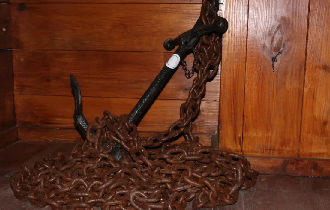 Antigua ancla con enorme cadena apoyada sobre una pared de madera